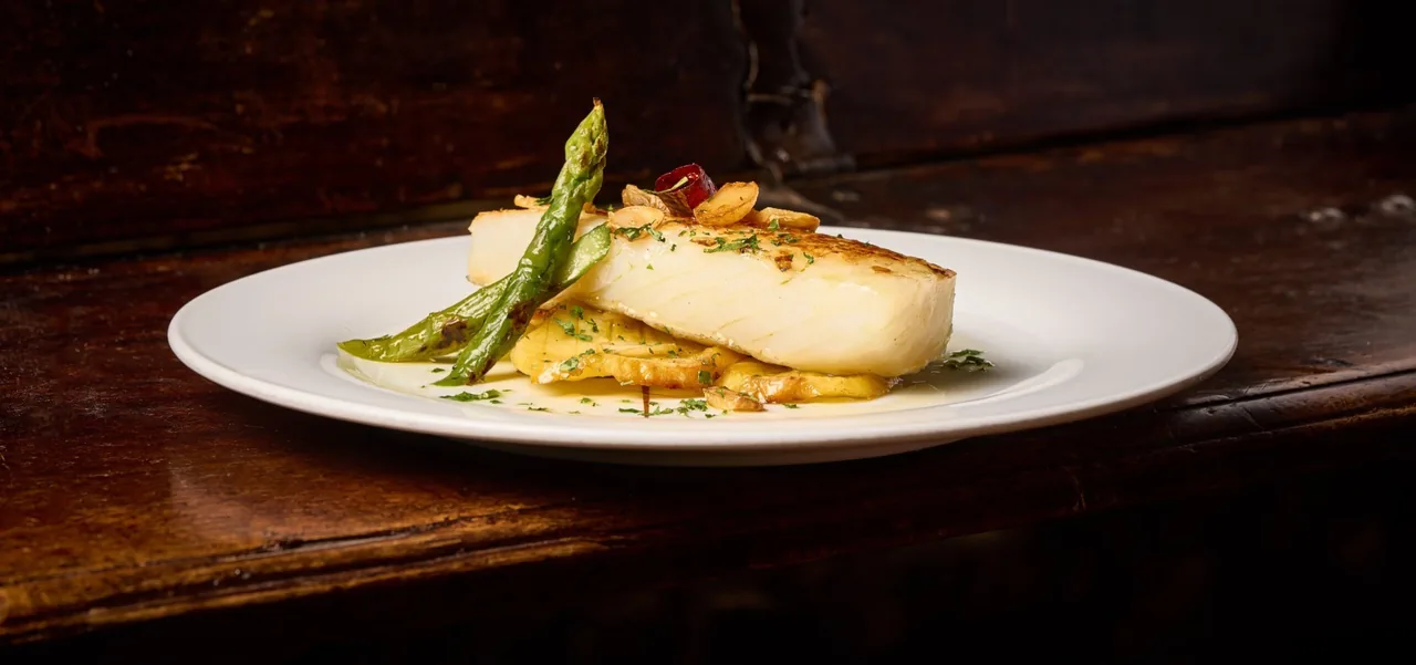 A white plate of a fish fillet with green peppers on a dark wooden surface