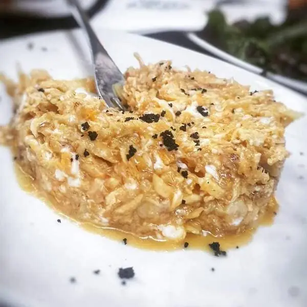 Broken/scrambled eggs dish in a golden sauce dusted with black flakes on a white plate, a fork resting in it