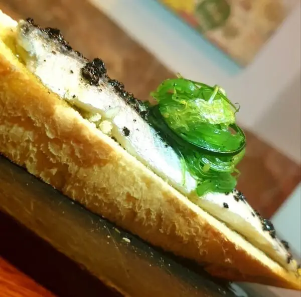 Open-faced toast topped with a marinated sardine fillet, black tobiko and a curl of green seaweed salad