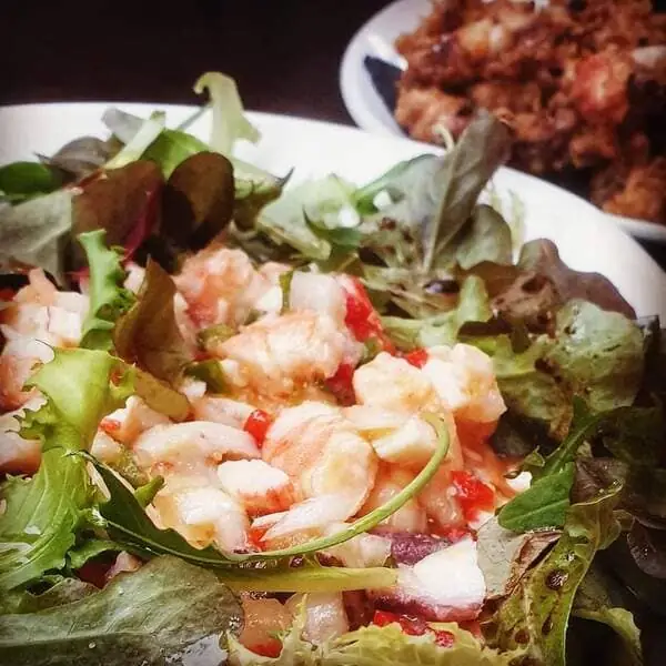 Prawn and mixed-leaf salad with red peppers on a plate, a fried dish blurred behind it