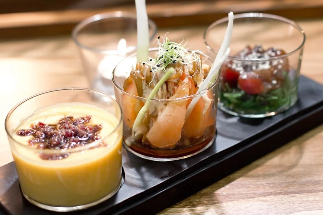 Three small glasses of tapas with sauces and toppings on a dark board