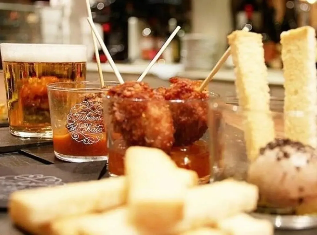 A table with a glass of beer, fried tapas on skewers and bread sticks