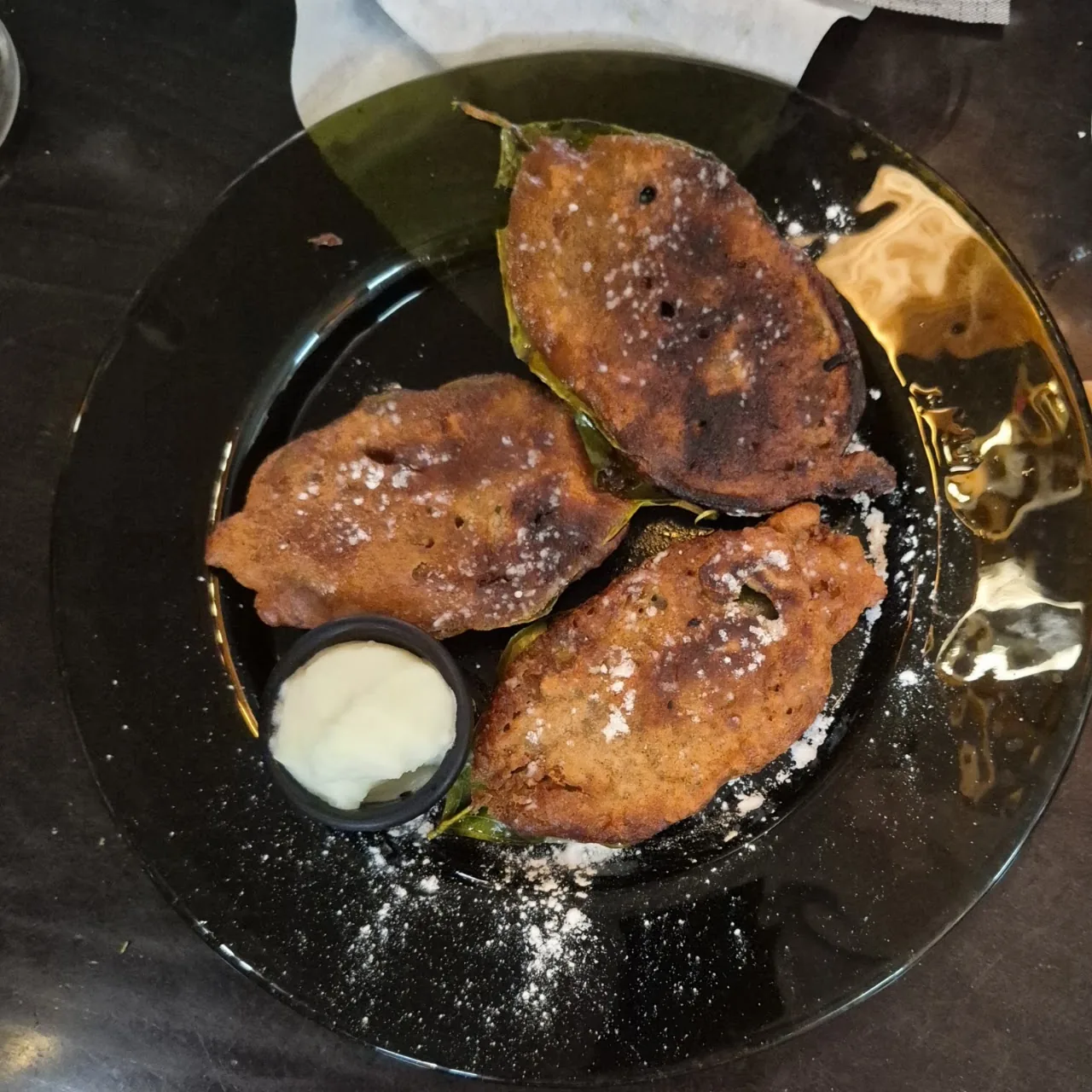 Two grilled fish steaks on a black plate with a dollop of cream