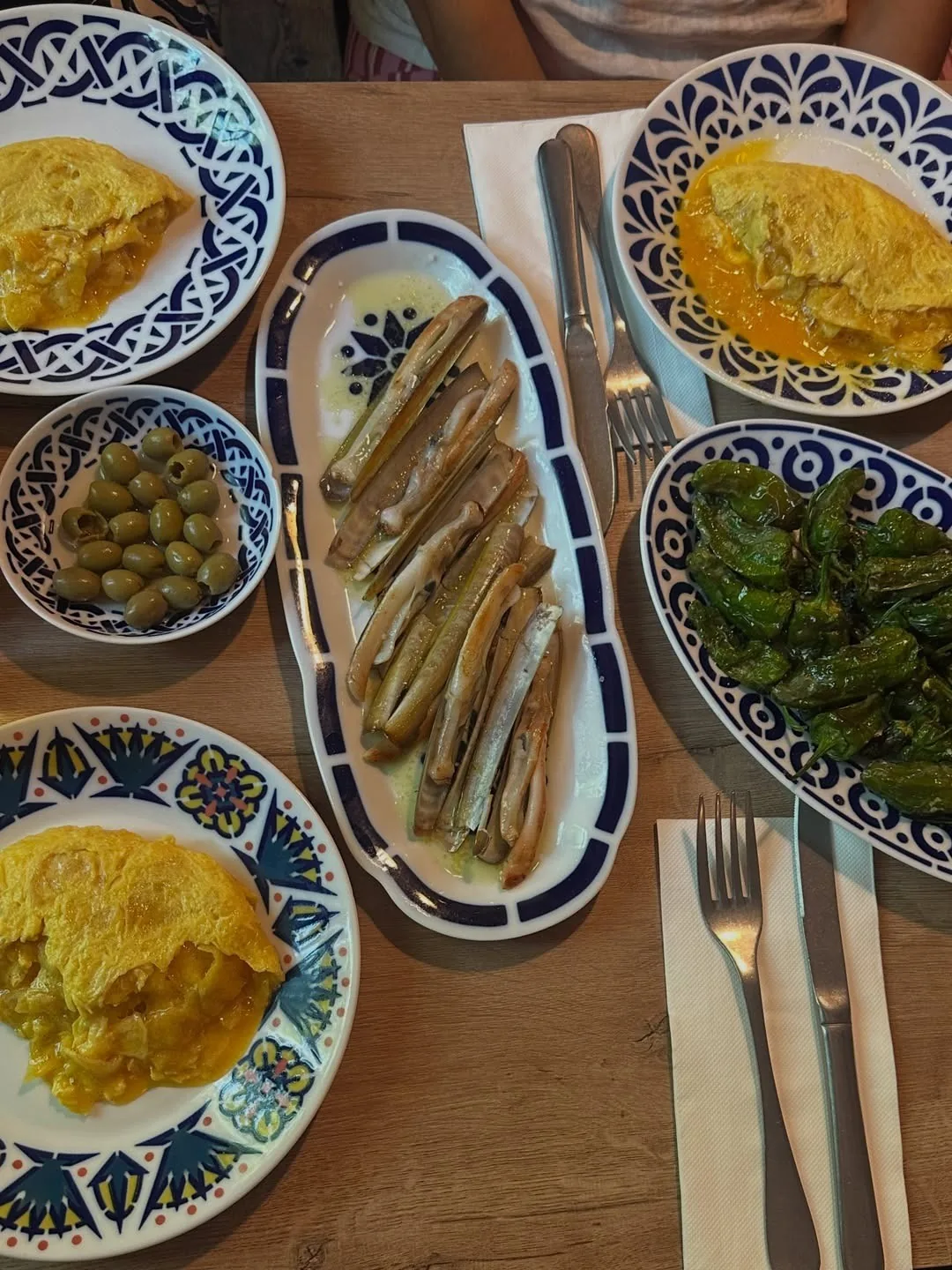 Several small dishes on a table including razor clams, green peppers and a tortilla