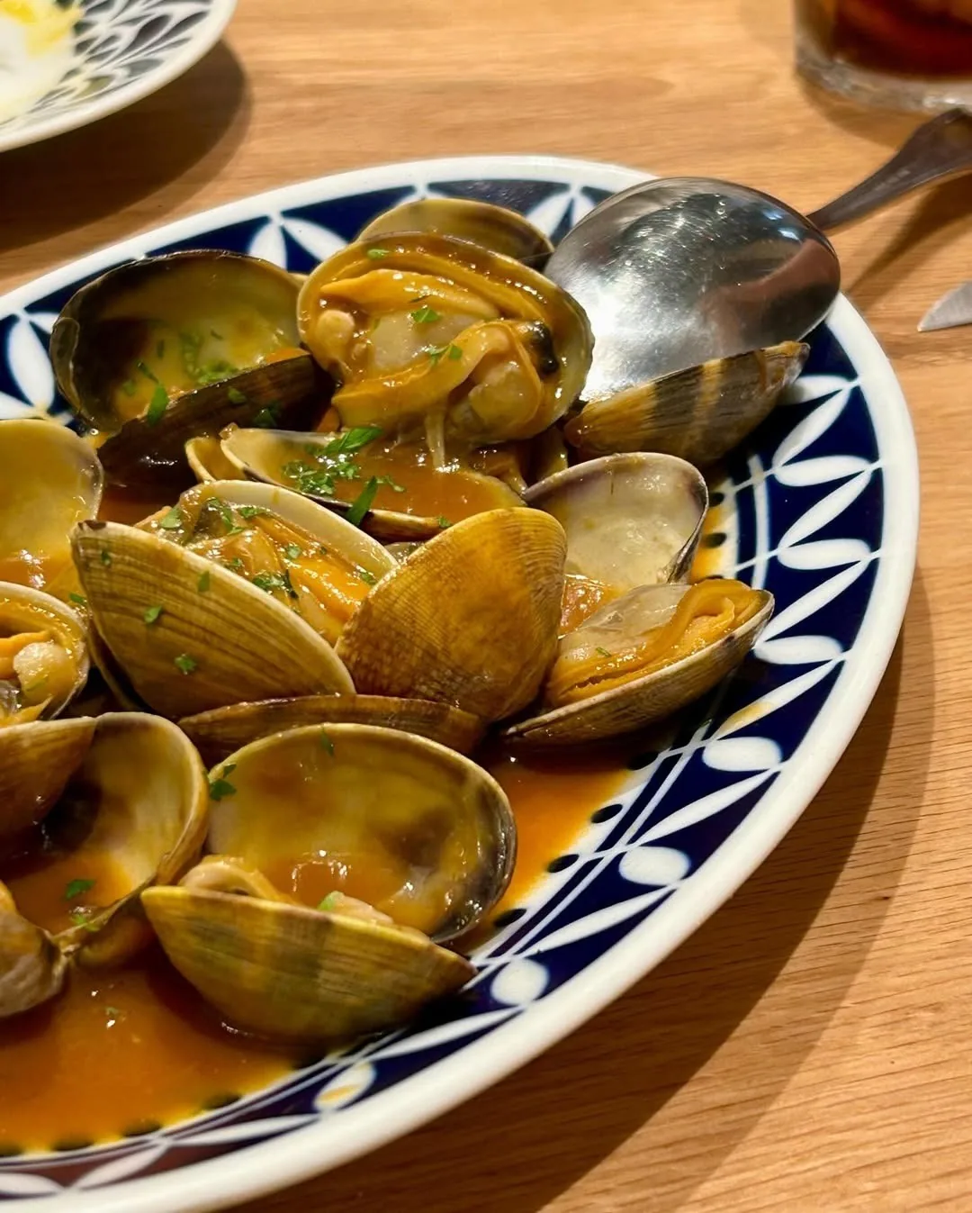 Clams in a golden broth on a blue and white oval platter