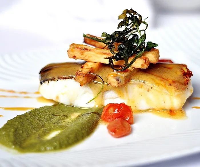 A seared fish fillet with green sauce and cherry tomatoes on a plate