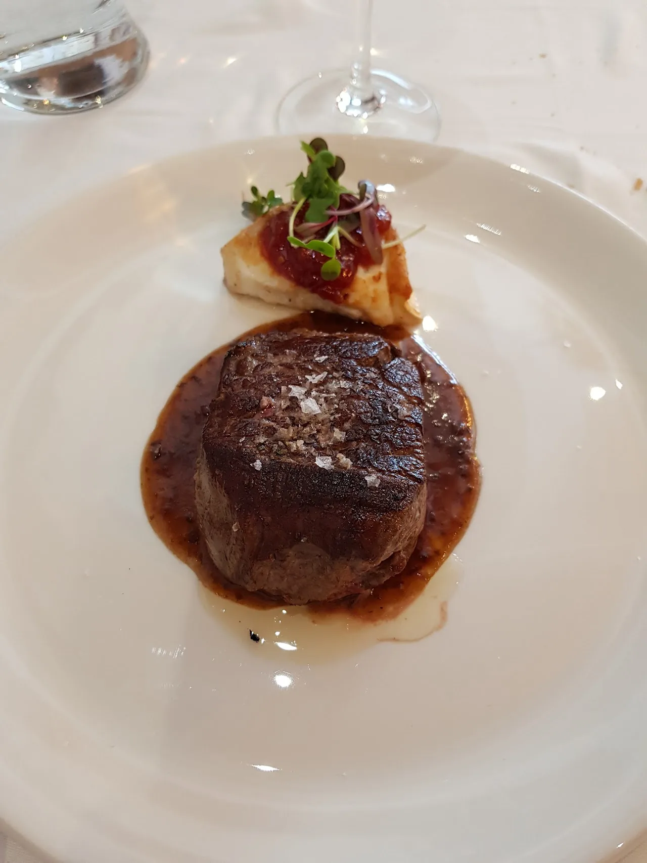 A seared steak medallion with a dark sauce on a white plate