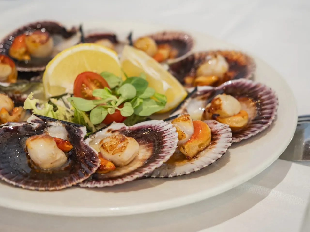 A plate of scallops on the half shell with lemon and greens