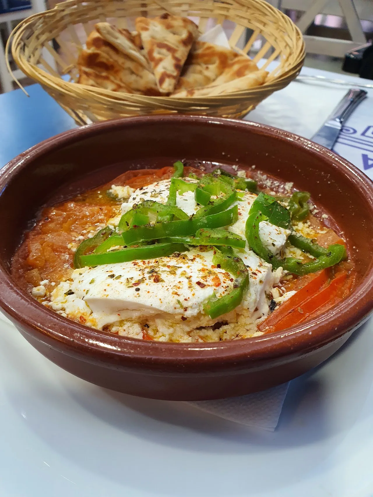 Baked feta cheese topped with green peppers in a clay dish