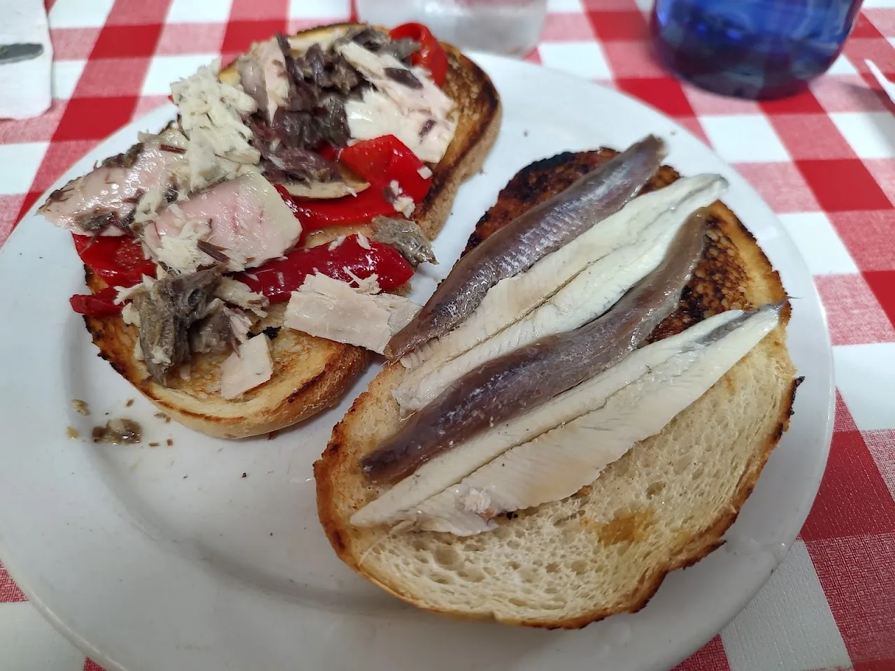 Two open-faced toasts topped with cured meat and anchovies