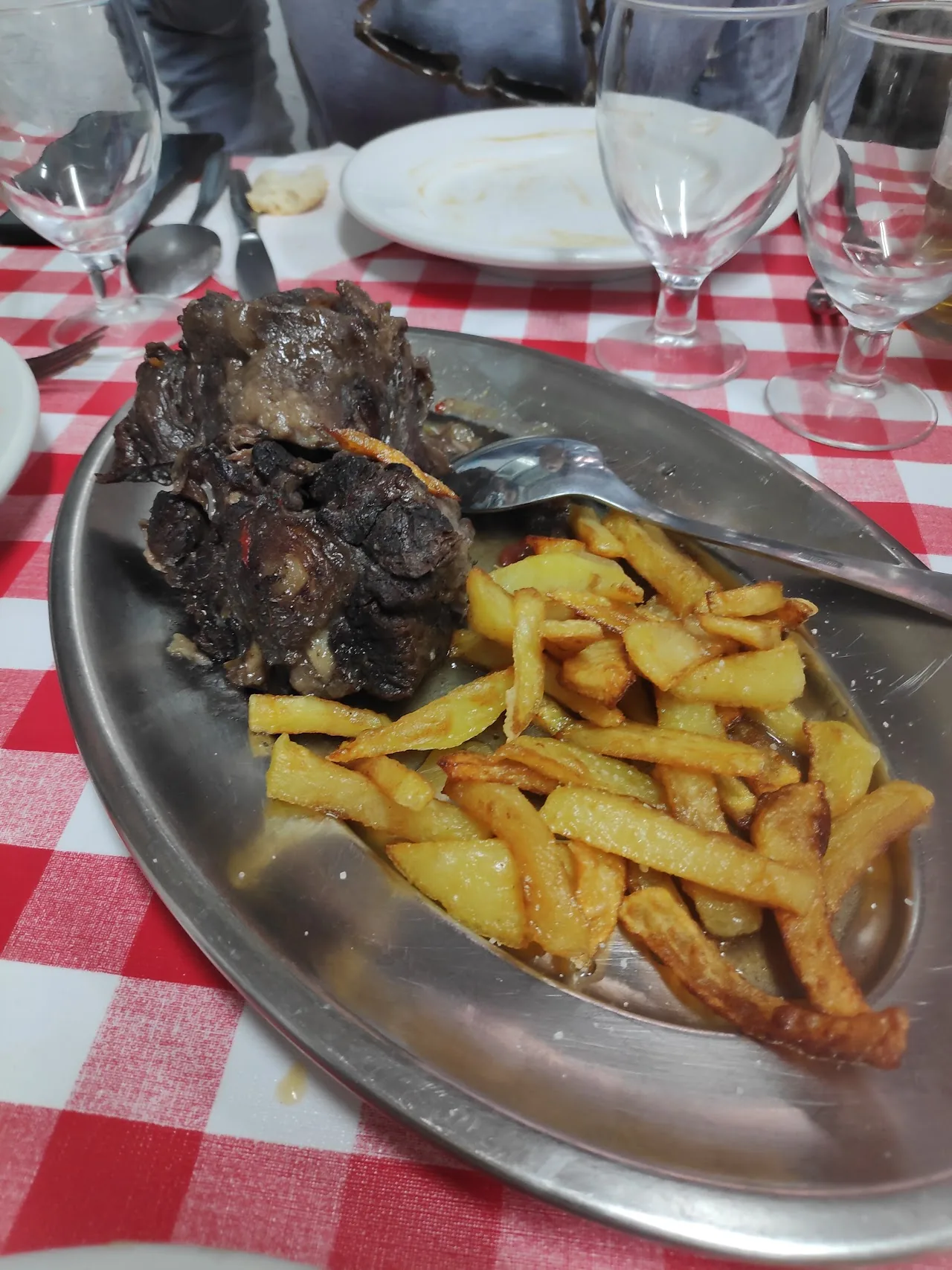 A metal tray of grilled ribs with fried potatoes