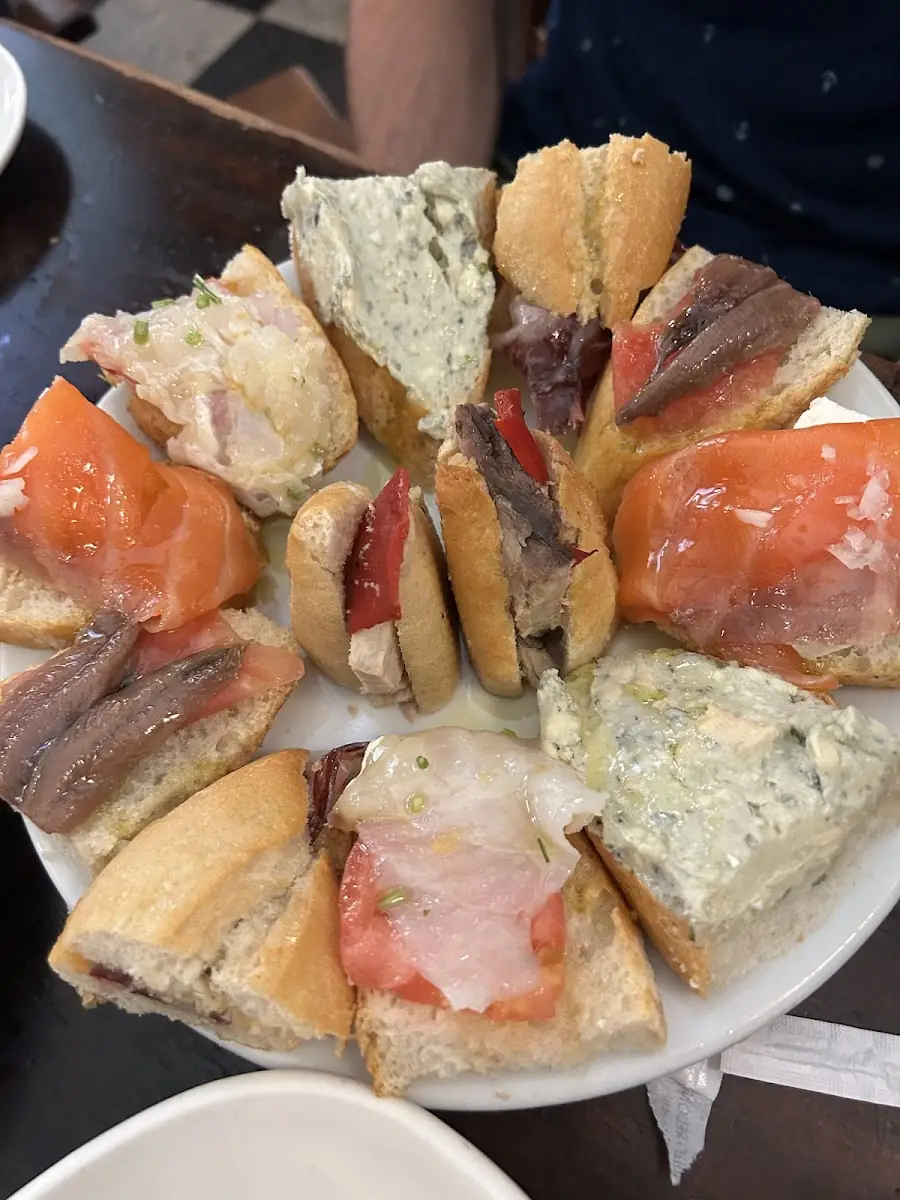 White plate arranged with assorted open-faced tapas on bread topped with anchovies, cured fish, blue cheese, tomato and salmon