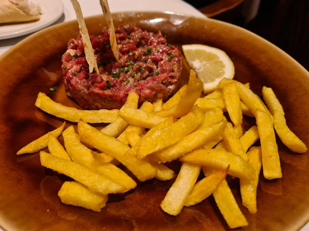 A mound of beef tartare with a lemon wedge and a side of fries