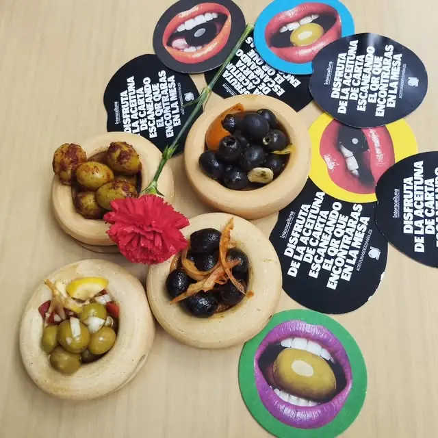 Several wooden dishes of green and black marinated olives arranged on a table amid printed promotional cards