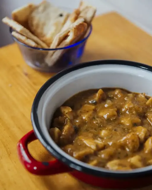 Stewed mushroom-and-meat dish in a red enamel pot with a bowl of pita crackers on a wooden table