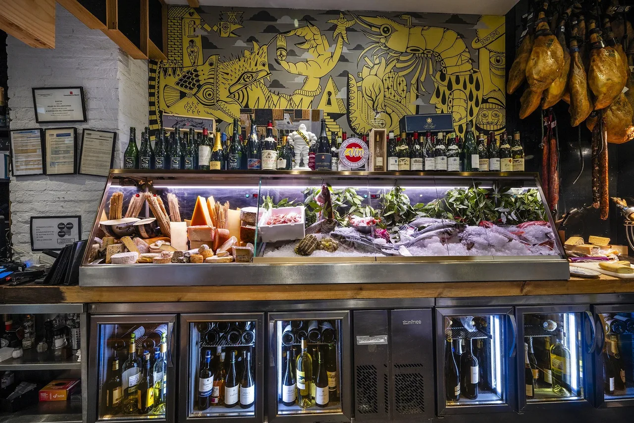 A restaurant interior with a counter, shelves of bottles and hanging hams on the back wall