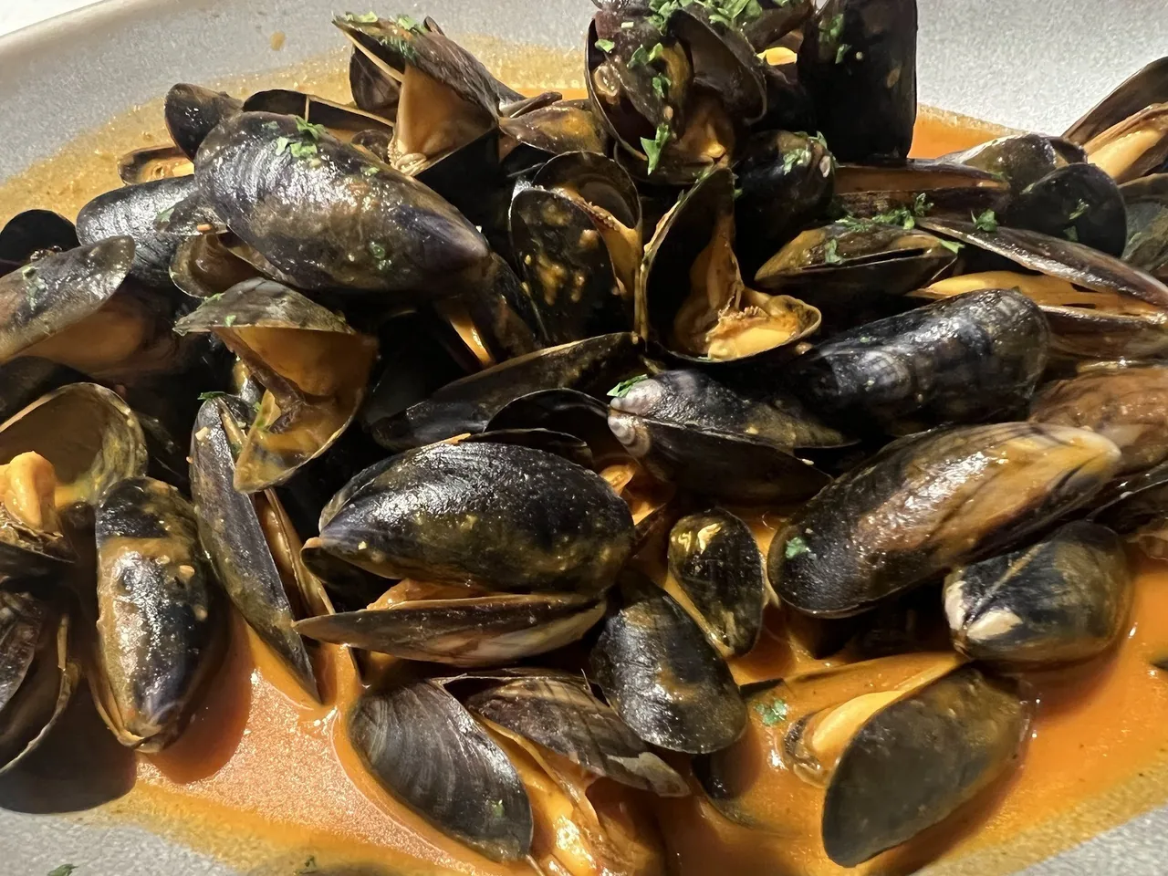 A dish of black mussels in an orange sauce