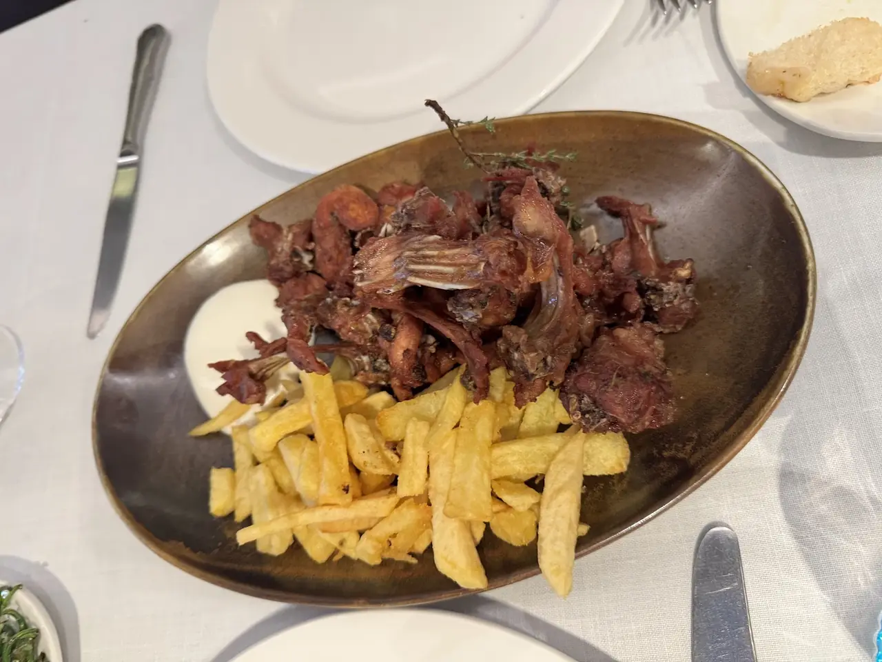 Fried meat pieces with herb garnish and a side of french fries on an oval dish