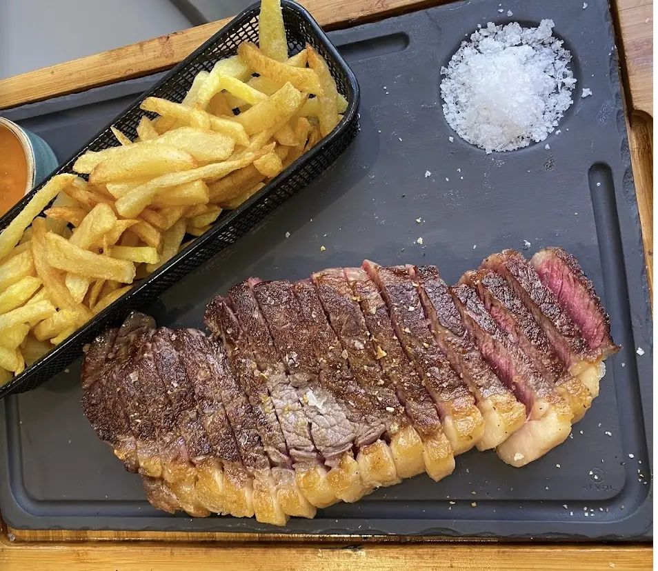 Sliced grilled steak with salt crystals next to a basket of french fries on a slate board
