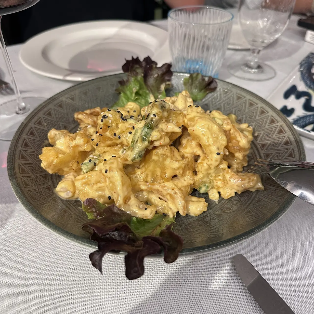 Battered seafood in a creamy spicy sauce with sesame seeds, plated with lettuce leaves
