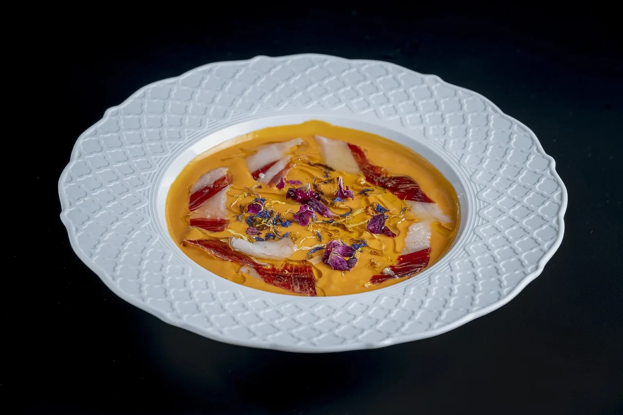 A creamy orange soup with toppings in a white patterned bowl on a dark background