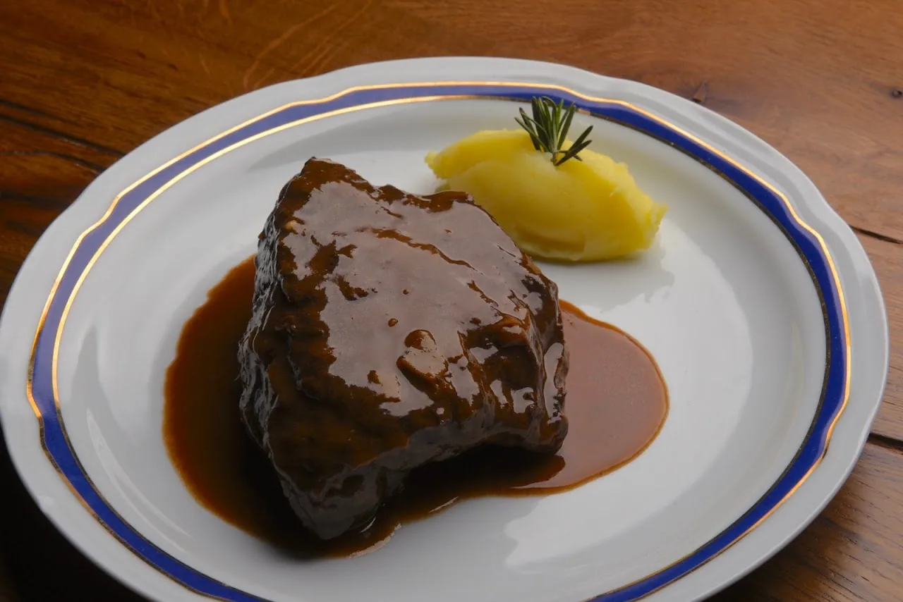 A braised piece of meat in dark sauce with a scoop of mashed potato