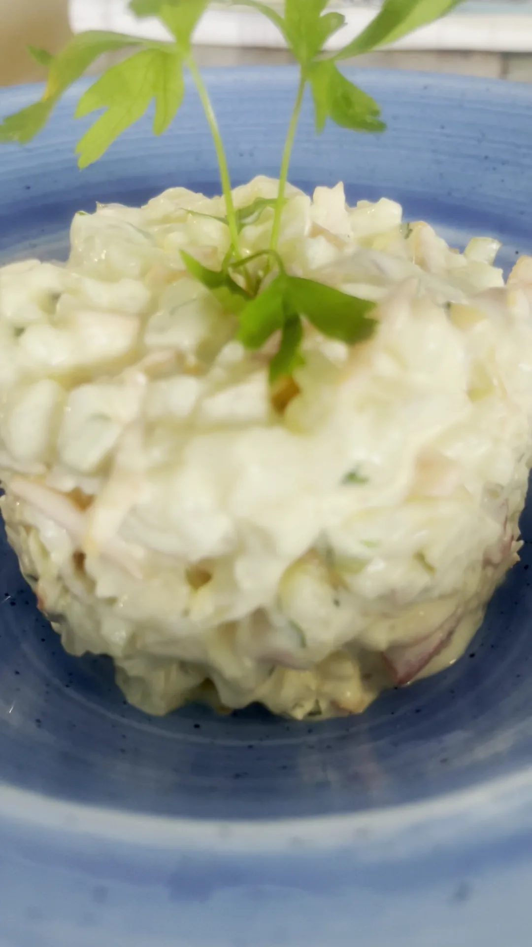A bowl of potato and vegetable salad garnished with a sprig of herb