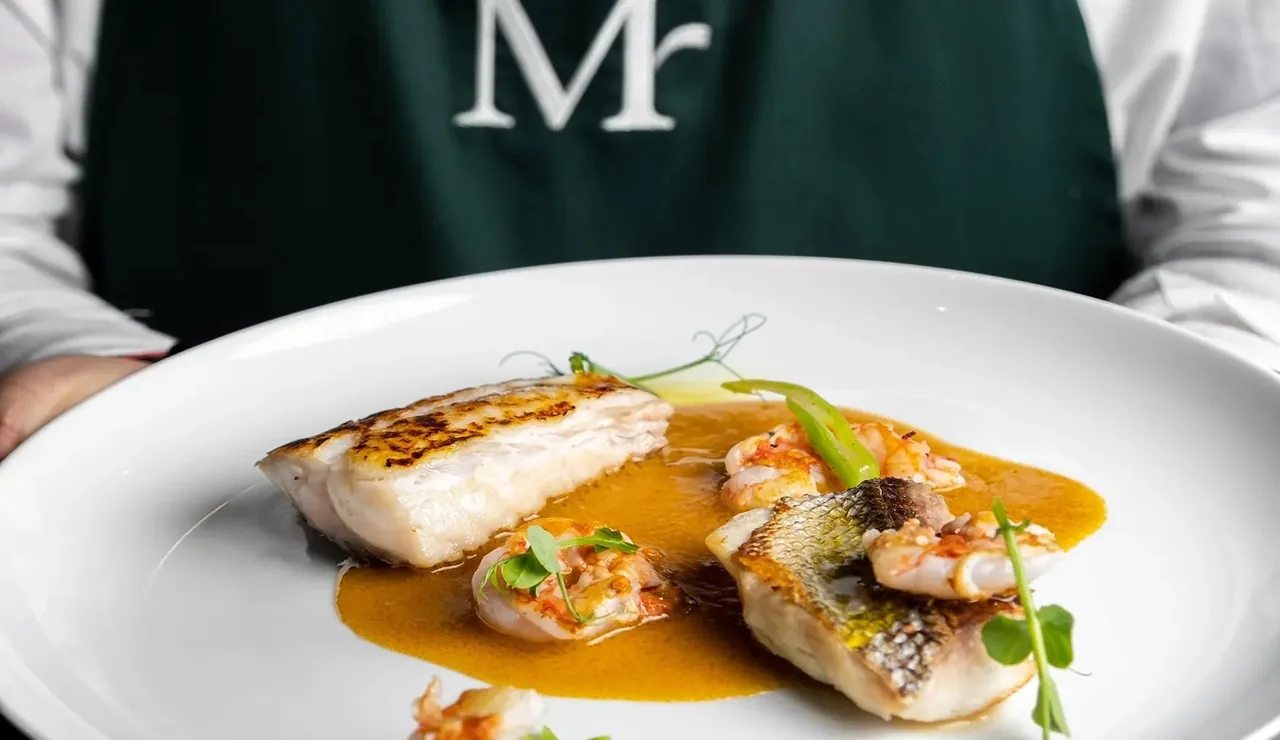 A white plate of seared fish with orange sauce and small vegetables