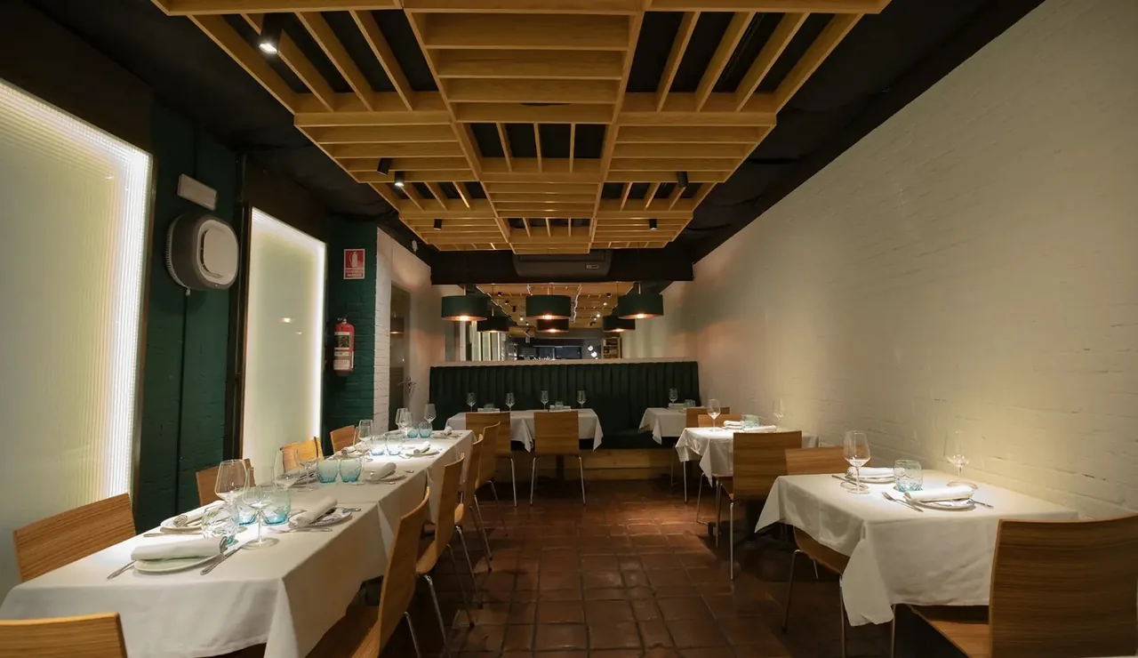 A long narrow dining room with tables set with white tablecloths