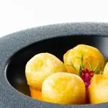 Golden fried croquette-style balls plated in a dark stone bowl over a pool of orange sauce