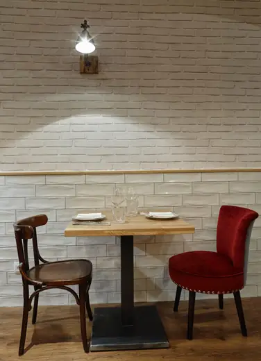 Single set table for two with a wooden bistro chair and a red velvet chair against a white-painted brick wall