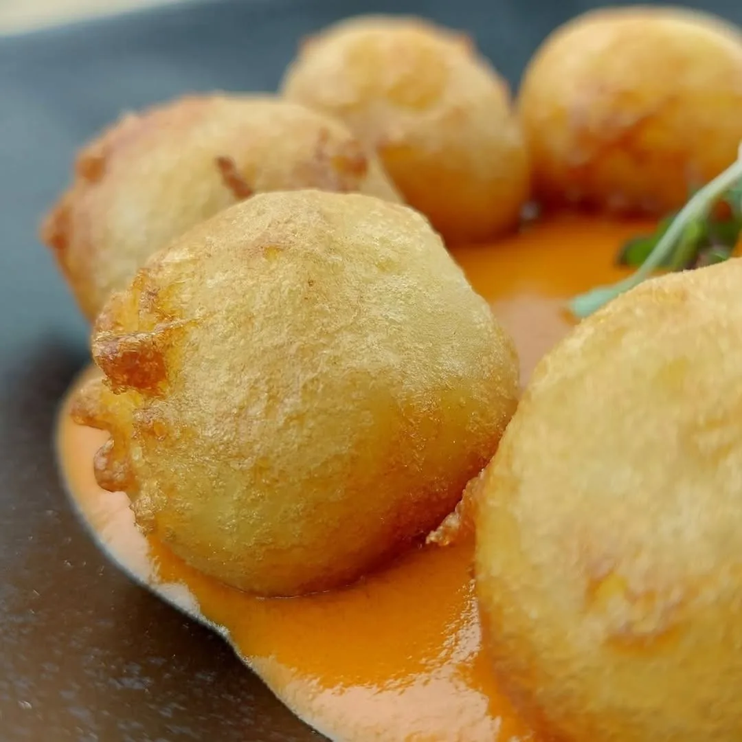 Golden fried potato balls in an orange sauce, seen close up