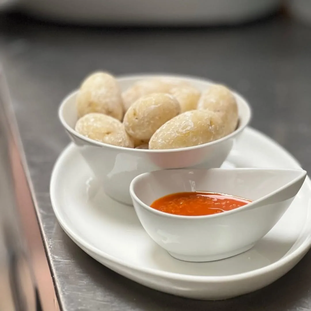 Small wrinkled potatoes in a white bowl beside a small dish of red sauce