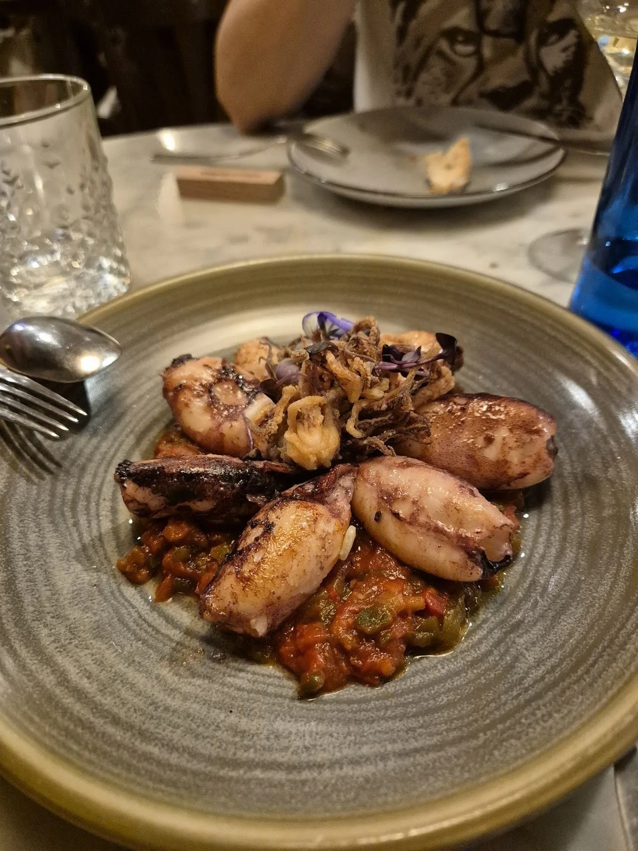 Small pieces of cooked squid on a grey ceramic plate with tomato sauce