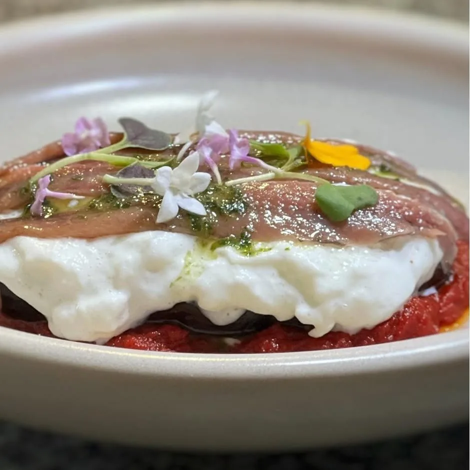 A white plate with anchovy fillets and white cheese over tomato, topped with small flowers