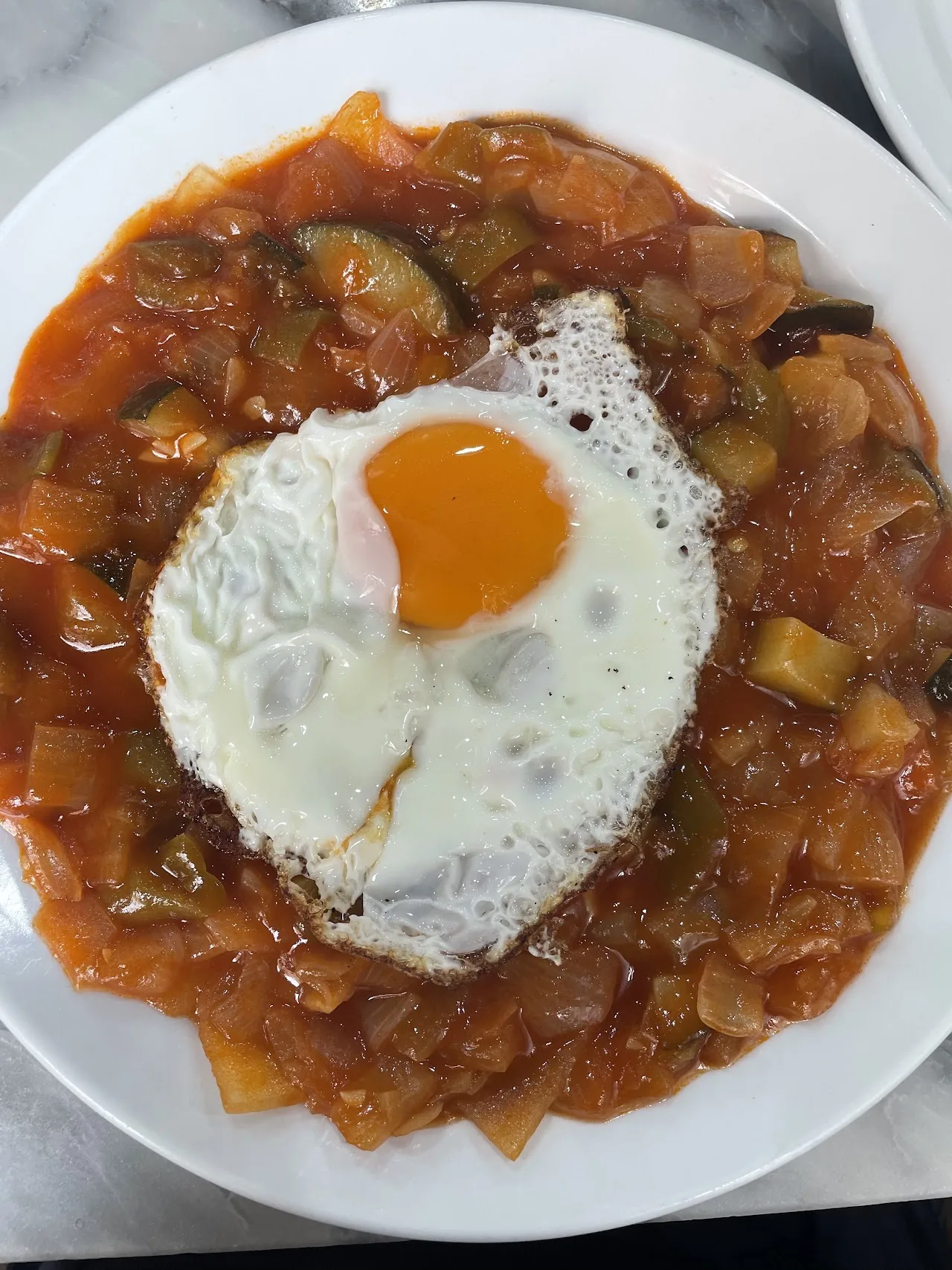 A fried egg atop a vegetable stew with a soft yolk
