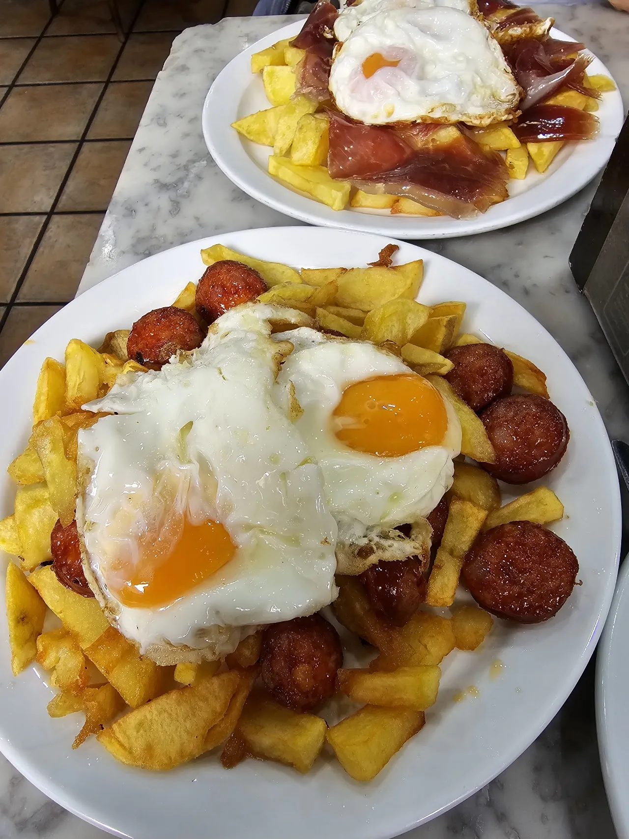 Fried potatoes topped with two fried eggs and chorizo, drizzled with sauce