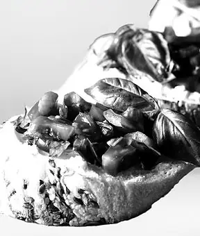 Black-and-white close-up of rustic bread topped with chopped vegetables and fresh basil leaves