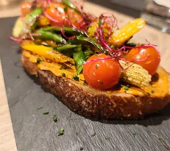 Vegetable tostada on grilled bread topped with cherry tomatoes, baby corn, green beans and micro shoots on a slate board