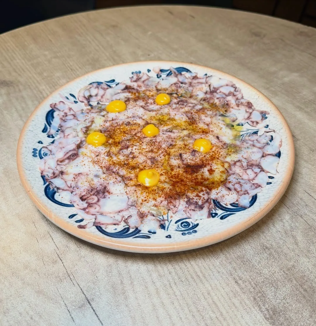A round patterned plate of thinly sliced seafood topped with egg yolk and paprika