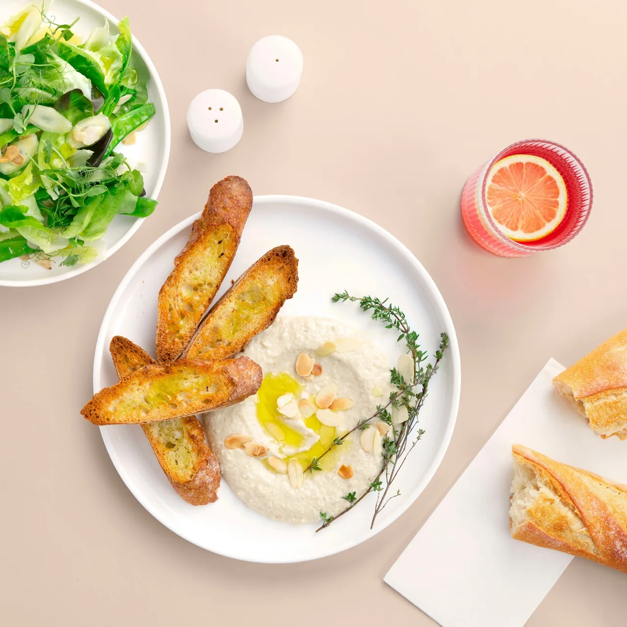 A plate of hummus with toasted bread slices and a green salad beside it