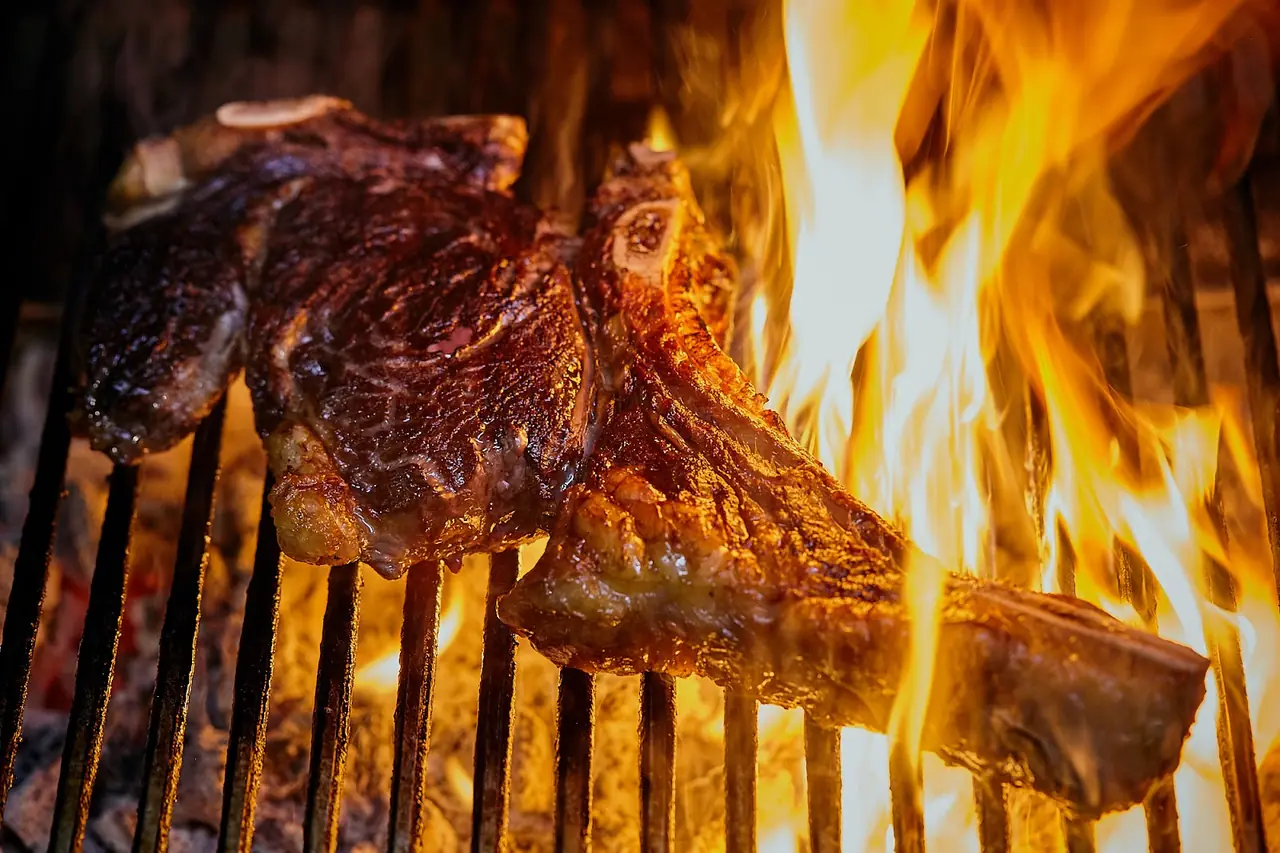 Bone-in chop searing over open flame on a charcoal grill