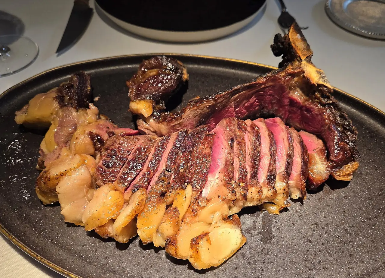 Sliced bone-in ribeye steak plated on a dark platter