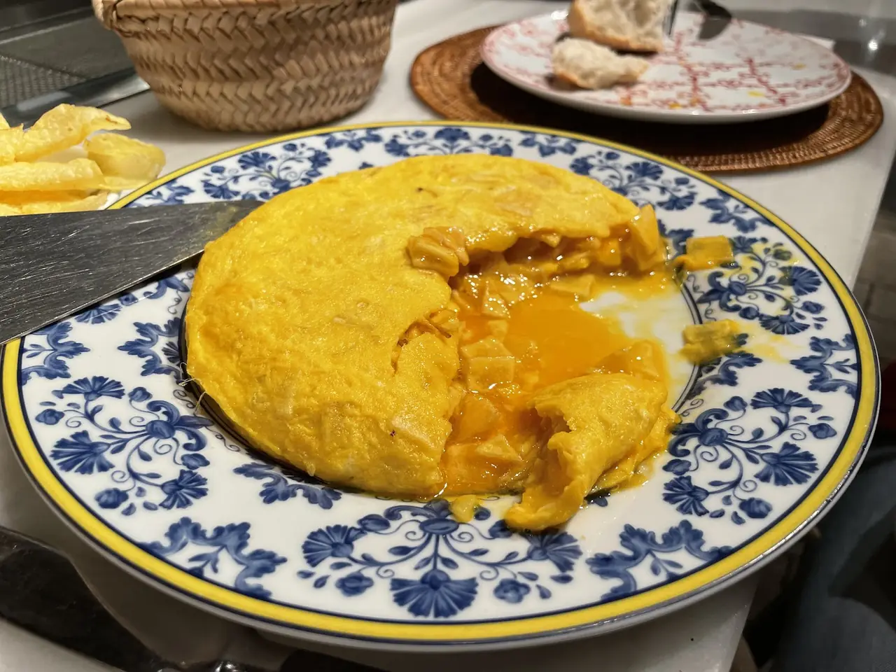 Runny Spanish tortilla cut open on a blue and white plate, egg spilling out