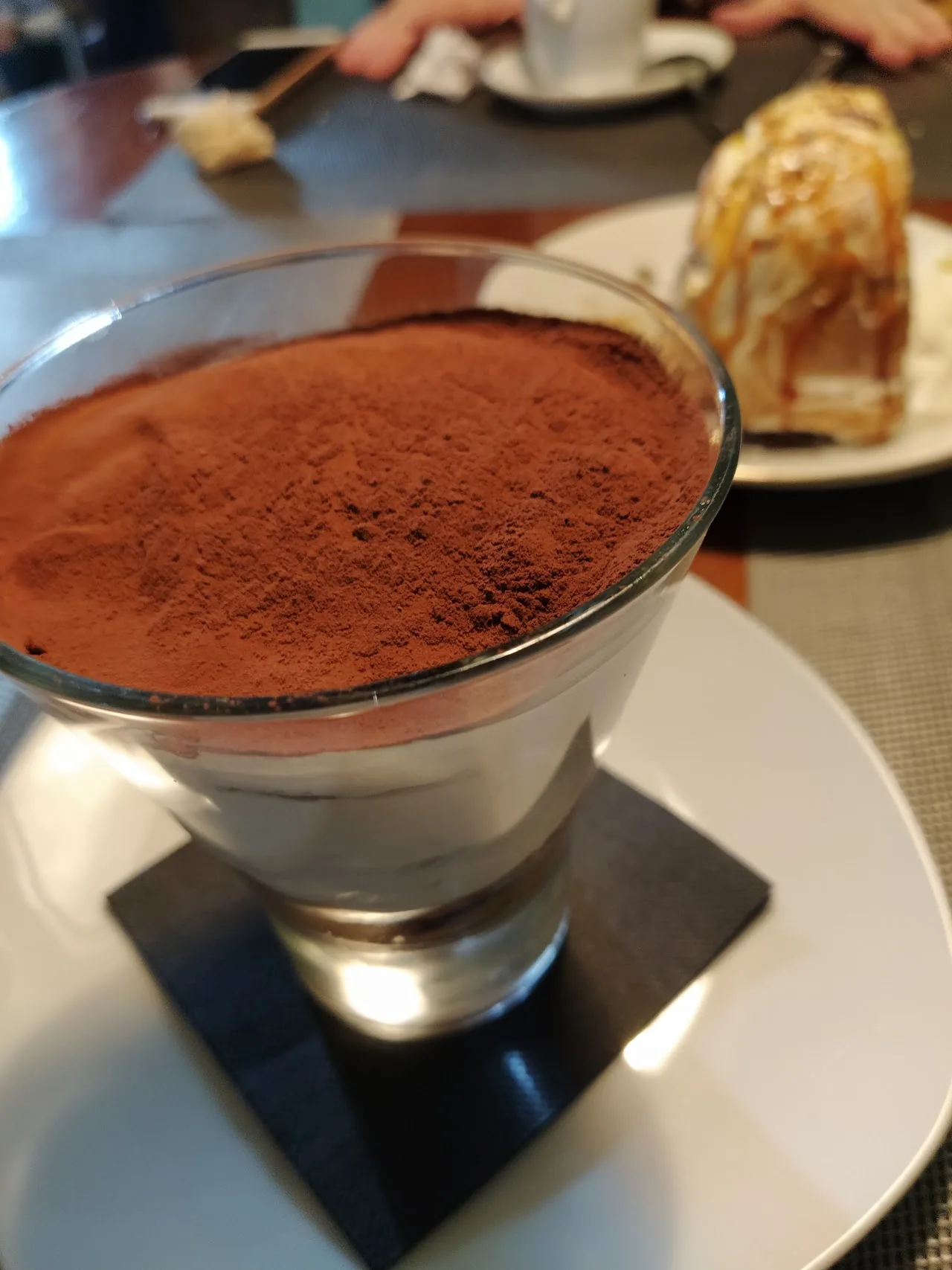 A tiramisu-style dessert topped with cocoa powder in a glass