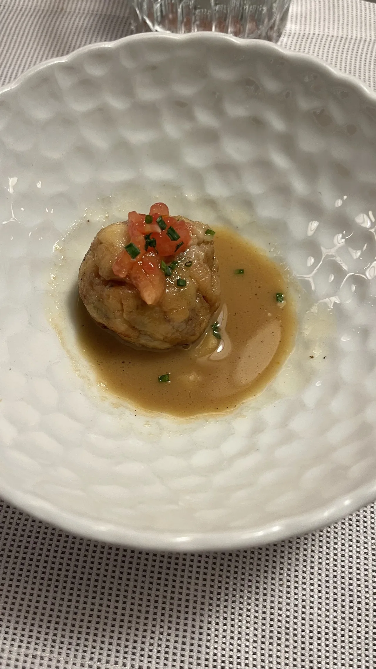 A round piece in a pale sauce with diced tomato in a white dimpled bowl