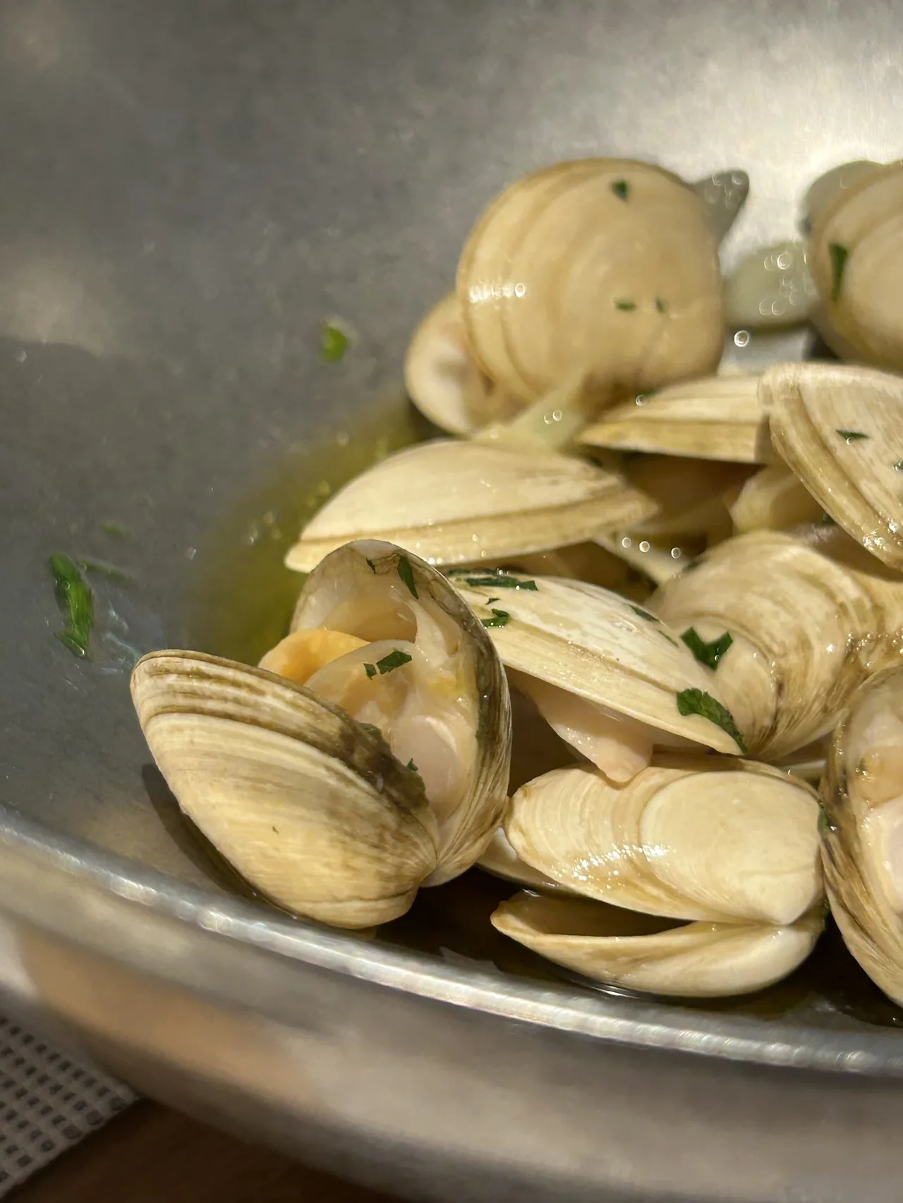 A metal dish of open clams in a green sauce