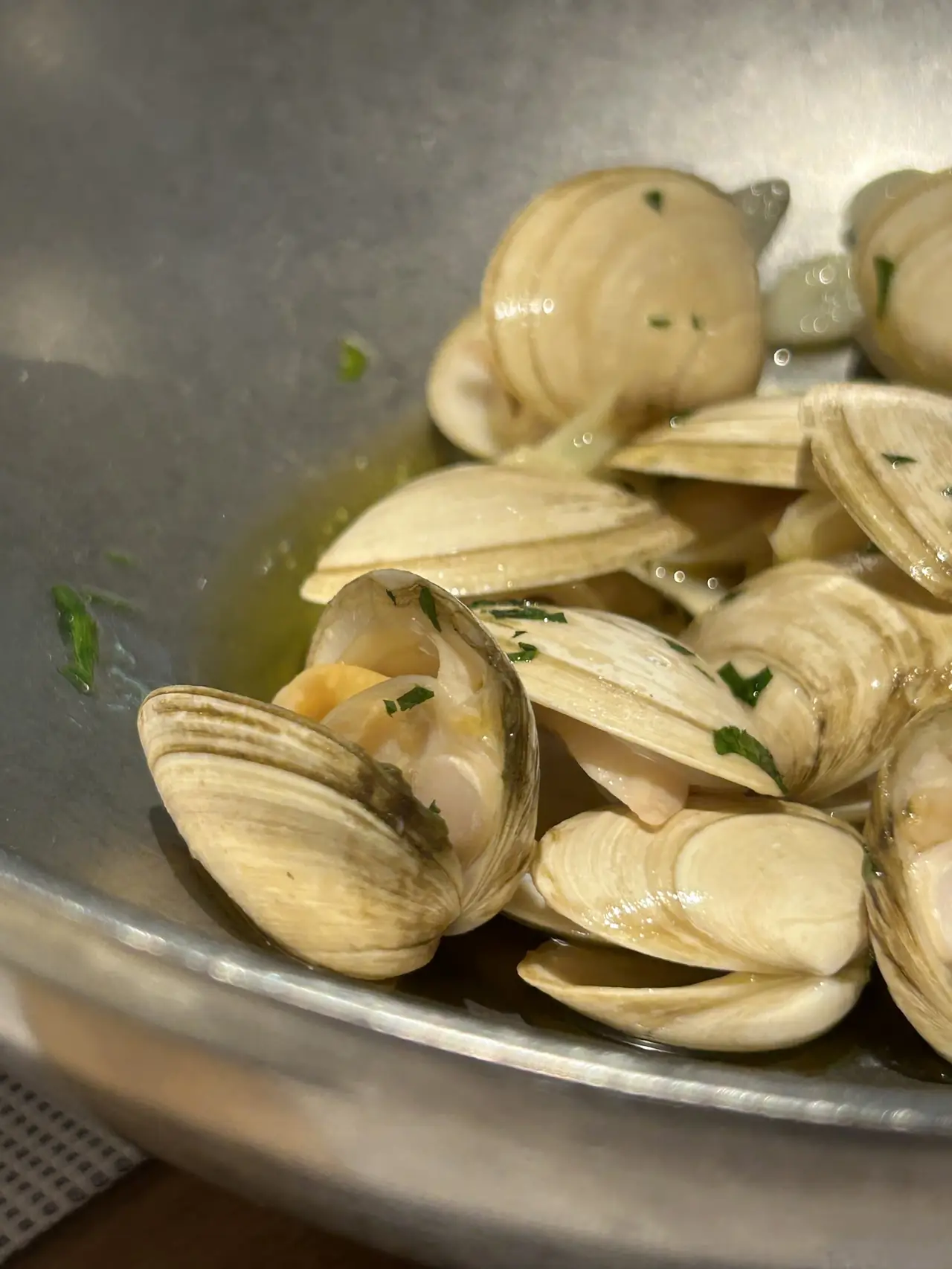 Steamed clams open in garlic and parsley sauce in a metal pan