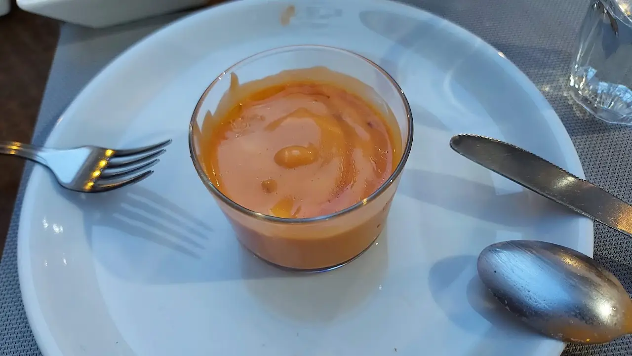 A small glass of orange soup on a plate with a fork and spoon