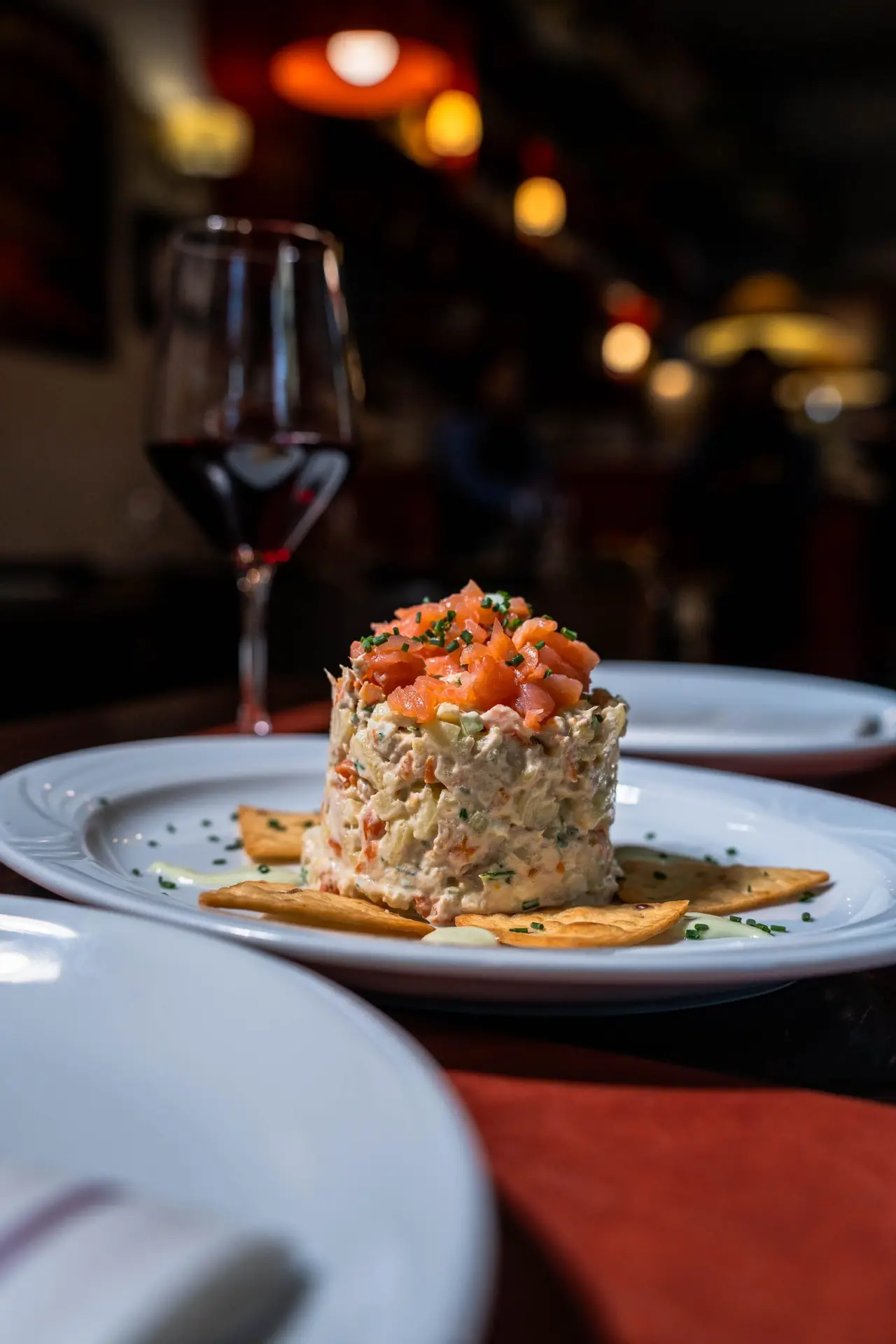 Seafood salad tower with tomato and mayonnaise, garnished with chives, wine glass in background